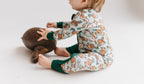 Child wearing a pair of zip-up pajamas with a pattern containing ducks and geese and playing with a wooden duck.