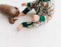 Child wearing a pair of zip-up pajamas with a pattern containing ducks and geese, sitting next to a wooden duck prop.