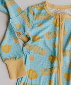 A baby long-sleeve zip-up sleeper in light blue with a gingham pattern and yellow butter-themed print, featuring yellow cuffs and a yellow zipper.