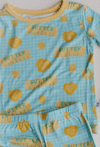 Flat lay of a toddler two-piece pajama set with a blue and yellow butter pattern against a plain white background.