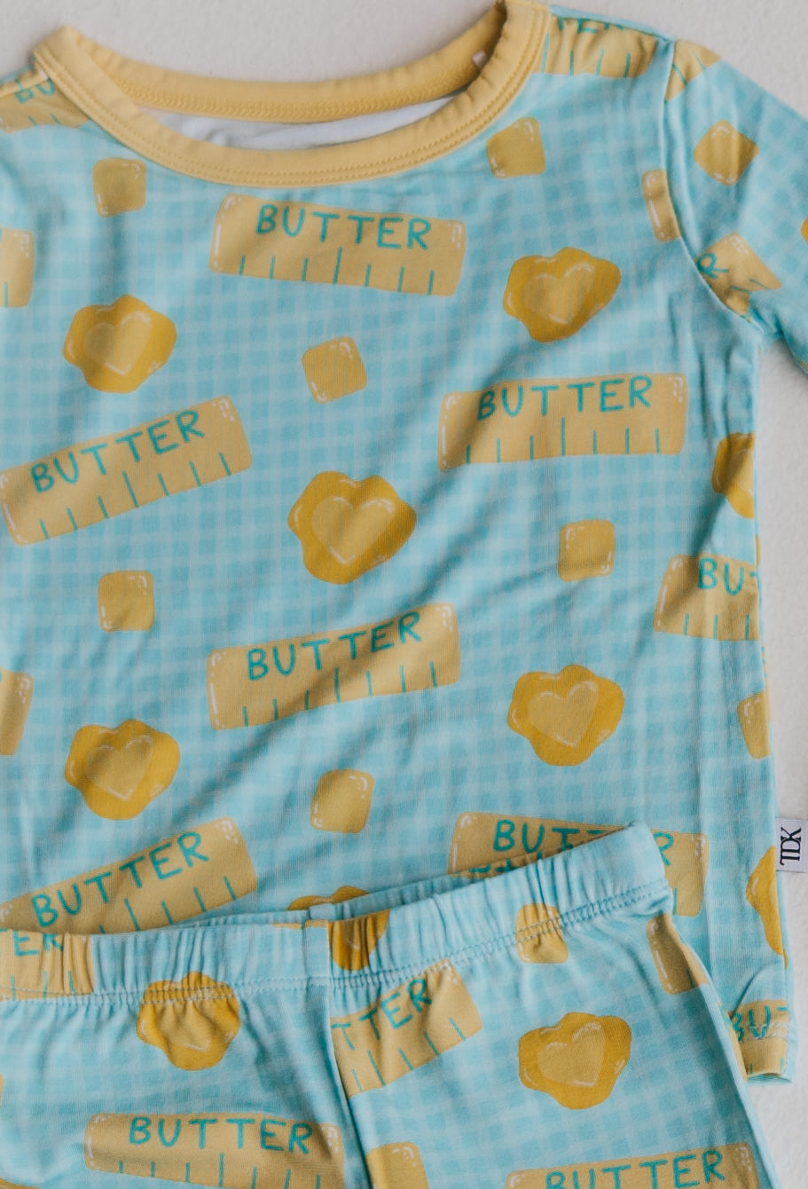 Flat lay of a toddler two-piece pajama set with a blue and yellow butter pattern against a plain white background.