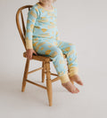 Child sitting on a small wooden chair wearing two piece pajamas set with a yellow and blue butter pattern against a plain white studio background.