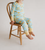Child sitting on a small wooden chair wearing two piece pajamas set with a yellow and blue butter pattern against a plain white studio background.