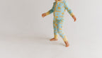 A baby wearing a light blue and yellow patterned long-sleeve footless pajama romper, walking barefoot on a plain white studio background.