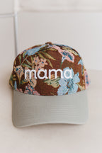A trucker-style baseball cap with a brown floral front panel and a light gray curved brim. The front panel features the word 'mama' embroidered in white across the center.