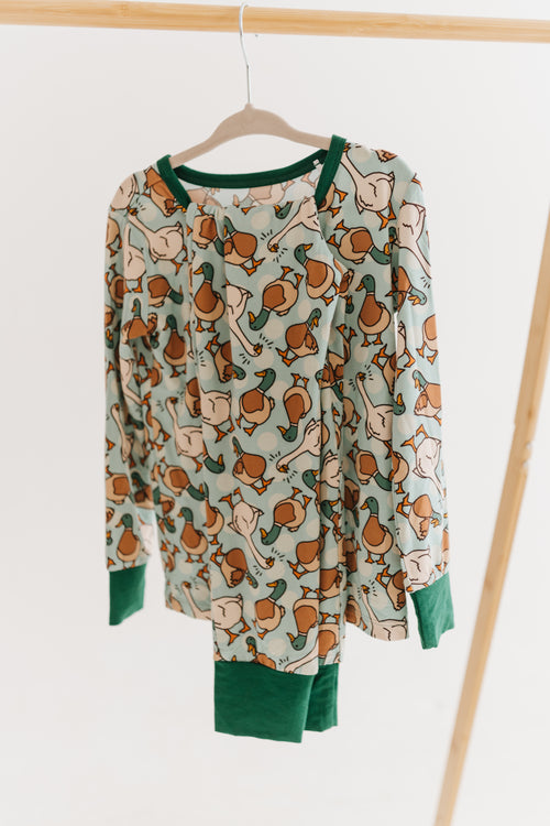 Two piece set of kid's pajamas with a duck and geese pattern hanging from a clothing rack with a plain white studio background.